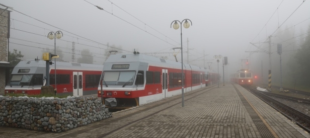Mlha zahalila stanici TEŽ a ozubnicové železnice na Štrbském Plese. Vedle stojících jednotek 425 965-1 a 425 954-5+425 963-6 proráží svými reflektory mlhu ozubnicová jednotka 405 951-5+905 951-0. | 11.7.2018