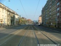 Středem Plzeňské ulice na zvýšeném tělese pokračuje tramvajová trať v klesání